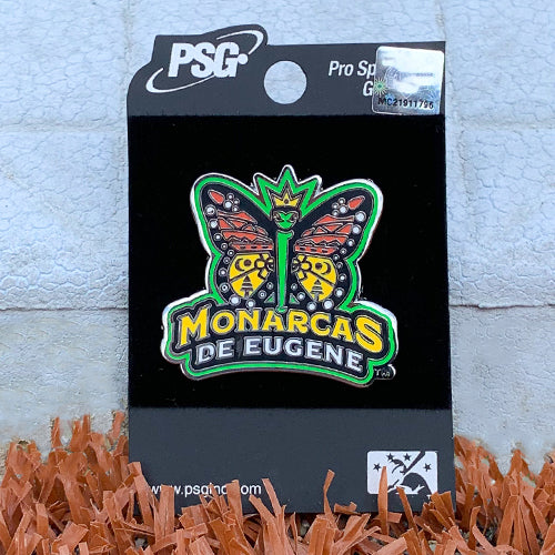 A silver lapel pin featuring the Los Monarcas logo. The Monarcas logo is a orange, yellow, and black monarch butterfly. The body and the outline of the butterfly is lime green. The butterfly is wearing a yellow three-point crown. Underneath the buterfly is the text "Monarcas" in yellow and "De Eugene" in white.